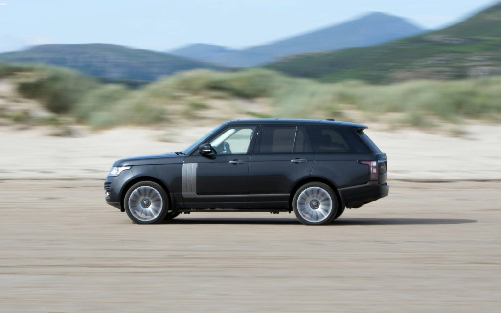 Black Range Rover Vogue driving along a beach with mountains behind